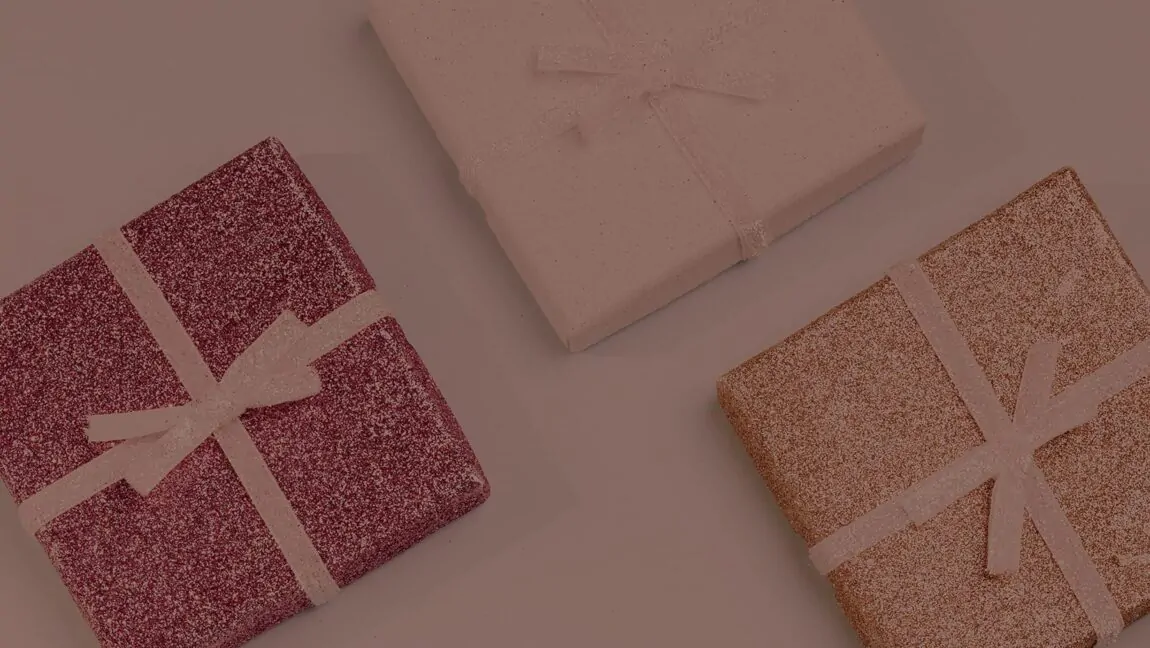 Três caixas de presente com glitter e laços delicados, em tons de rosa, dourado e lilás, sobre fundo neutro