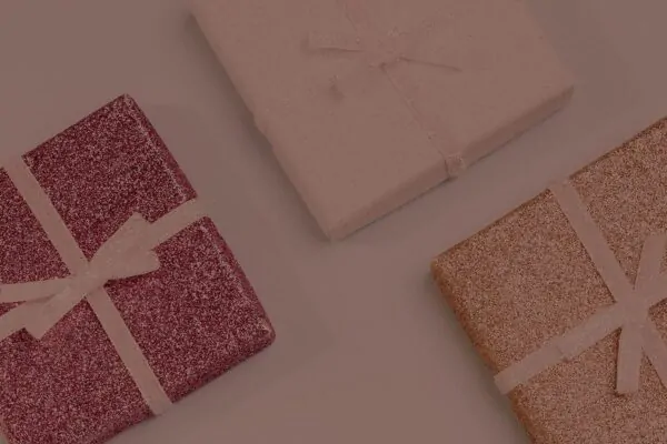 Três caixas de presente com glitter e laços delicados, em tons de rosa, dourado e lilás, sobre fundo neutro