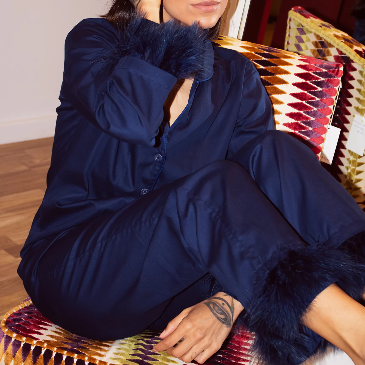 Mulher sentada usando pijama personalizado azul-marinho com detalhes de plumas nos punhos e barras, em tecido 100% algodão com toque acetinado.