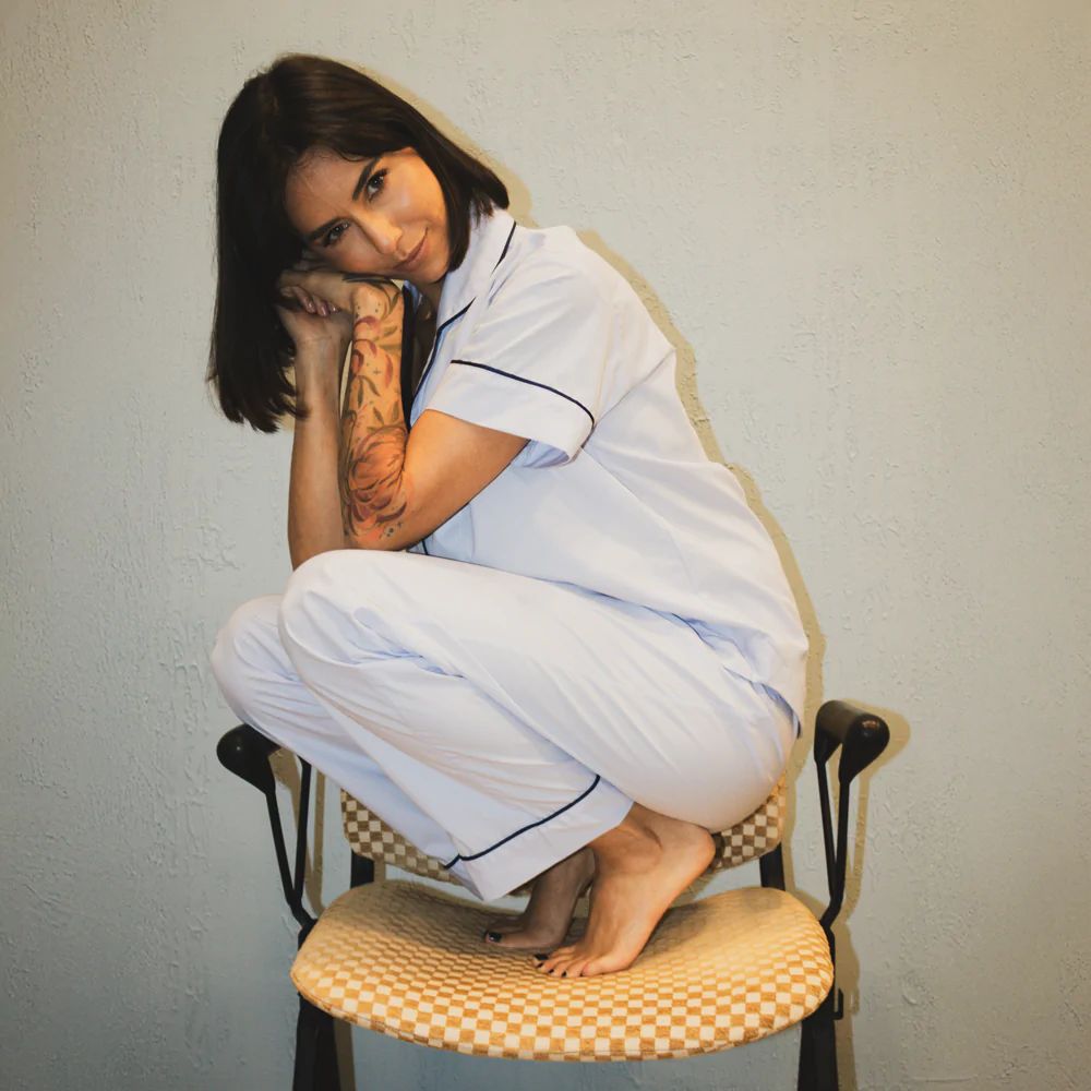 Mulher usando pijama personalizado azul bebê de manga curta e calça, em tecido 100% algodão com acabamento azul-marinho, sentada sobre uma cadeira.