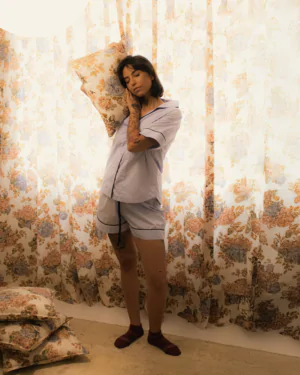 Mulher usando pijama personalizado azul bebê de manga curta e shorts, em tecido 100% algodão com acabamento azul-marinho, encostando o rosto em uma almofada floral.