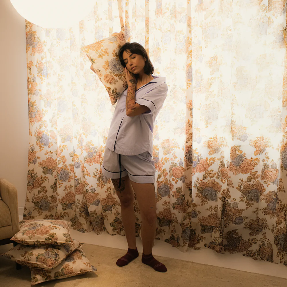 Mulher usando pijama personalizado azul bebê de manga curta e shorts, em tecido 100% algodão com acabamento azul-marinho, encostando o rosto em uma almofada floral.