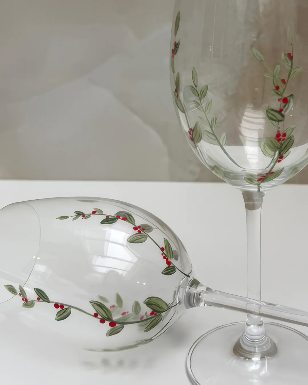 Detalhe de taças de cristal pintadas à mão com ramos, folhas verdes e pequenos frutos vermelhos, estampa Voo Sereno da Naps